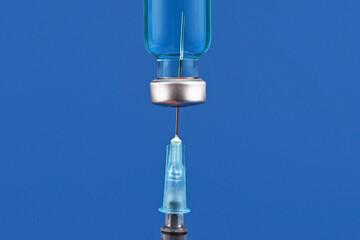 Close up of syringe drawing up blue liquid from medical vial on dark blue background