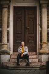 Fototapeta na wymiar Influencer sitting on the stairs of an old building and posing with hand on her chin.