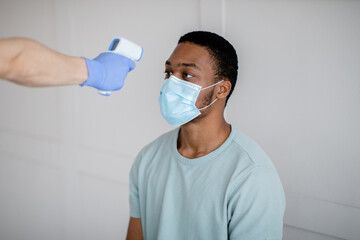 Doctor or nurse using infrared thermometer to measure temperature of black male patient before...