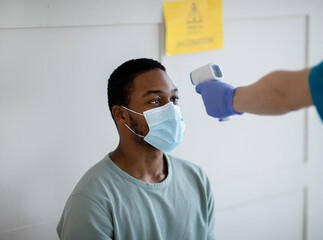 Black man having his temperature measured by infrared thermometer at clinic before getting covid-19...