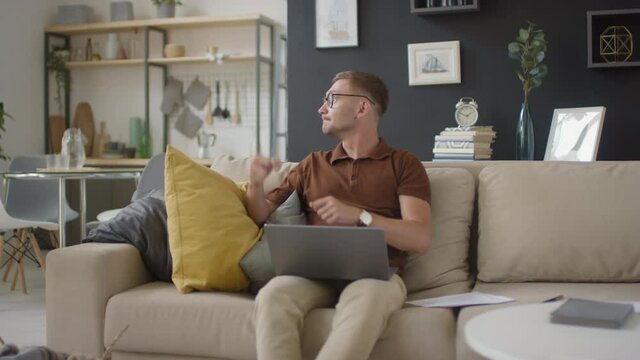 Medium front-view footage of busy man working from home typing on laptop while his little active son playing, running around and having fun disturbing father