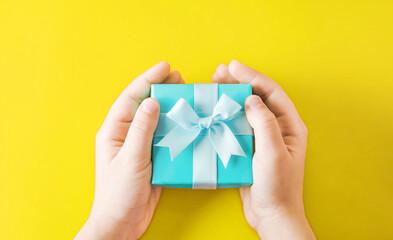 Child's hands holding turquoise gift box on yellow background
