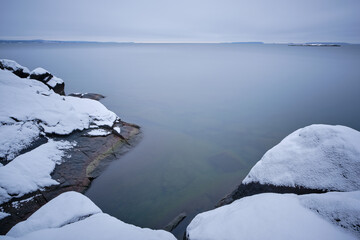 Long exposure of snowy cliffs by the sea with the horizon in the background