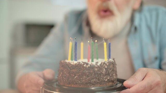 Aged man blowing out candles on birthday cake, celebrating life event, tradition