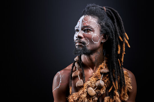 shaman tribal ritual man isolated in studio, exotic aborigen with ethnic make-up on face, shirtless african male with dreadlocks