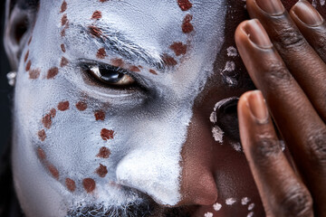 black male with national ethnic make-up on face, pagan eyes look at camera close-up, closing half of face
