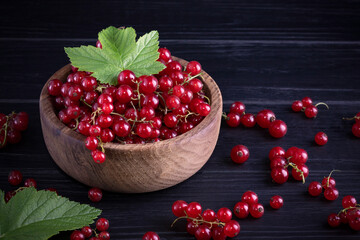 Red currant and green leaves on a dark wooden background. Background with currant berries and green leaves. Currant Macro.