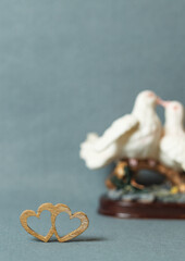 Naklejka premium Two wooden hearts joined together and Statuette with kissing pigeons in the background, selective focus