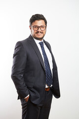 A young Latino businessman wearing glasses and standing in a dark suit and tie on a white background