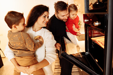 Joyful family with little kids at the kitchen. Caring mother and father cooking with wonderful children, smiling. Beautiful parents with son and daughter baking cookies, weekends concept