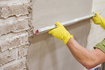 Construction worker  plastering and smoothing concrete wall with cement for brick imitation. Renovation at home. repairing  walls. Builder using plastering tool for finishing wall