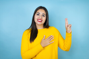 Young beautiful woman wearing yellow sweater over isolated blue background smiling swearing with...