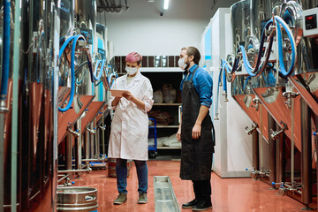 Young female brewery expert entering data in tablet with male brewer near by
