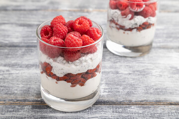 Yogurt with raspberry, goji berries and chia seeds in glass on gray wooden background. Side view, selective focus.