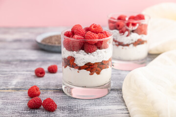 Yogurt with raspberry, goji berries and chia seeds in glass on gray wooden background. Side view, selective focus.
