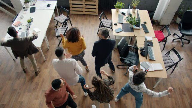 High angle view of joyful people coworkers dancing having fun and laughing in workplace together. Modern lifestyle and cheerful youth concept.