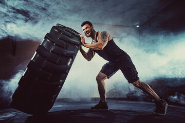 Bodybuilding training, bearded strong sportsman with muscular body lifting heavy wheel in gym.