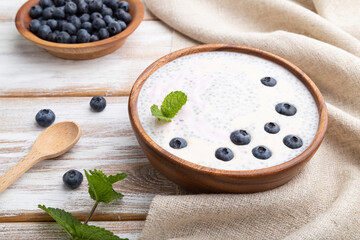 Yogurt with blueberry in wooden bowl on white wooden background. Side view.