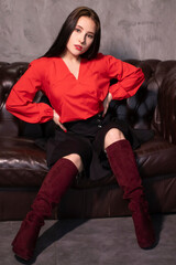 portrait of attractive brunette woman in red blouse and black skirt sitting on leather couch in a vintage cafe. st valentines day.