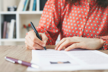 Woman at office desk signing a contract with shallow focus on signature.