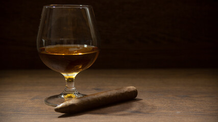 BOURBON GLASS WITH CIGAR ON RUSTIC WOOD TABLE AND LITTLE LIGHTING, WITH SPACE FOR TEXT