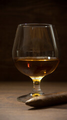 BOURBON GLASS WITH CIGAR ON RUSTIC WOOD TABLE AND LITTLE LIGHTING, WITH SPACE FOR TEXT