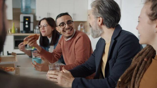 Diverse group of people coworkers are talking and laughing eating pizza in workplace enjoying work break together. Emotions and business concept.