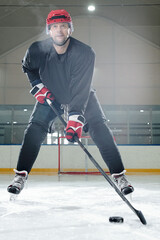 Mature hockey player in sports uniform, helmet and gloves going to shoot puck
