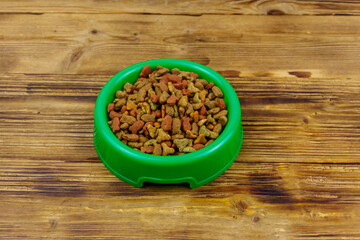 Dry food for cat or dog in bowl on wooden background. Pet food on wood surface