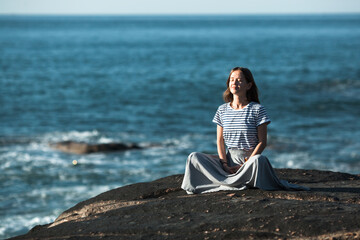 Woman meditates in the lotus position on the ocean coast. Yoga training.