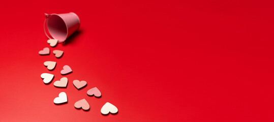 Creative flat lay of heart shape objects on bright red background falling from pink bucket