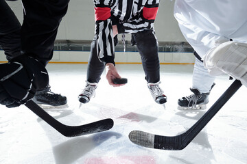 Hockey referee with puck standing on rink with two rivals on his right and left
