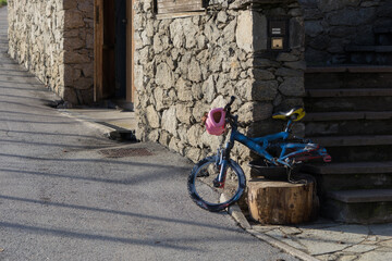 Colorful childs bicycle in front of an old natural stone wall, nobody on the street