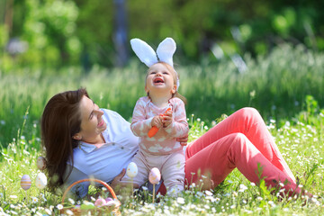 Happy family celebrate Easter, smiling and having fun at blooming meadow. Mother play with funny child wearing rabbit ears with basket with eggs, carrot outdoors. copy space. Egg hunt. Easter concept