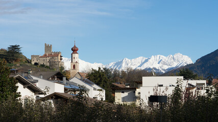 Picturesque mountain landscape in Naturns in South Tyrol in autumn, in the fore an old church, castle and old buildings and in the background the snow-covered Alps, no people