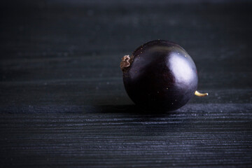 Black currant and green leaves on a dark wooden background. Background with currant berries and green leaves. Currant macro.