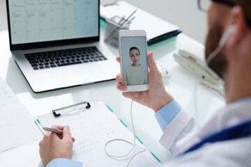Female patient on smartphone screen looking at doctor with medical document