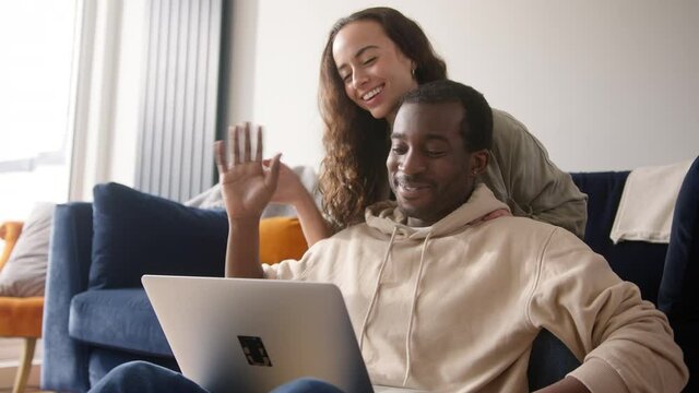 Relaxed Young Couple At Home Sitting On Sofa Making Video Call On Laptop Computer