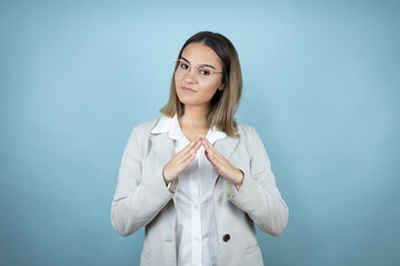 Young business woman over isolated blue background with Hands together and fingers crossed smiling relaxed and cheerful. Success and optimistic