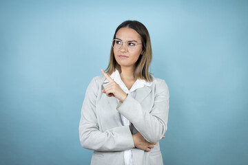 Young business woman over isolated blue background confused and pointing with hand and finger to the side