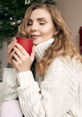 Blonde woman in white woolen sweater drinking hot coffee