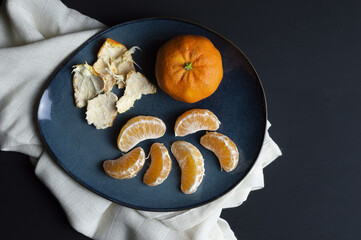 top view of a single mandarin whit segments and peel in a blue plate on a white towel on black...
