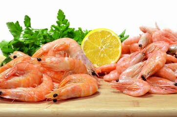 Boiled shrimp with lemon and fresh herbs on a wooden cutting board on a white background