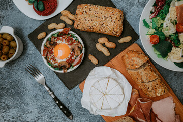 Perfectly cooked fried eggs with mushrooms, spices, pepper, meat and salt on arugula. Round breakfast plate on black plank with peanuts and baguette with seeds