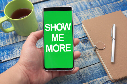 Show me more, text words typography written on smart phone against wooden background, life and business motivational inspirational