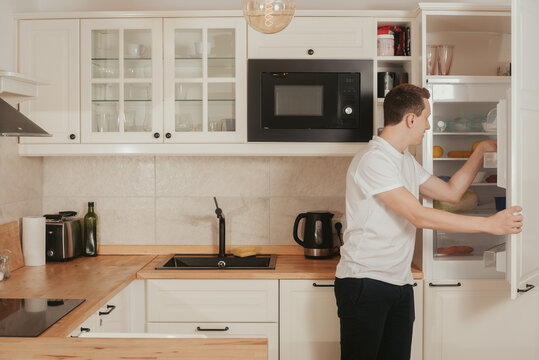 The man is standing in the kitchen. The guy is hungry, gets food from the refrigerator. The guy prepares his own food. The man puts something in the refrigerator.