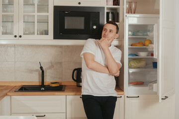 A man stands in the kitchen and looks into the refrigerator, does not know what to eat, thinks what to cook for dinner, breakfast, lunch. The bachelor guy is cooking. Healthy food delivery