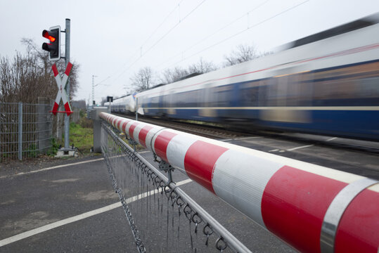 Selective focus view at red and white level crossing railway barrier and blur moving train on the rail on countryside in Germany in winter season during cloudy day. 