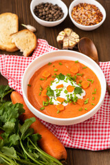 Delicious traditional carrot soup with herbs and sour cream on a wooden table.