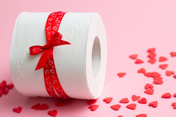 Roll of toilet paper as gift for Valentine's Day, next to red hearts on pink background, copy space